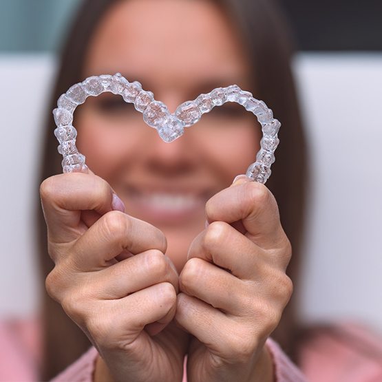 A woman making a heart with Invisalign aligners